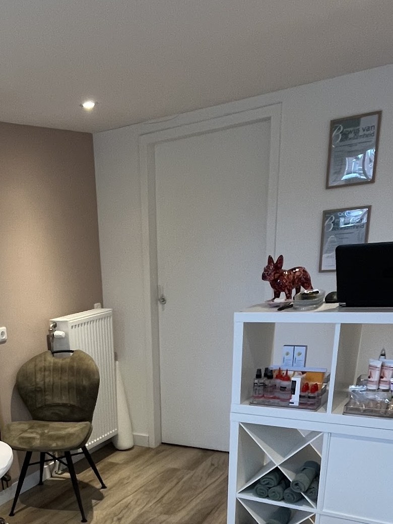 Een hoek van de salon met een stoel, een witte kast met handdoeken en verzorgingsproducten
